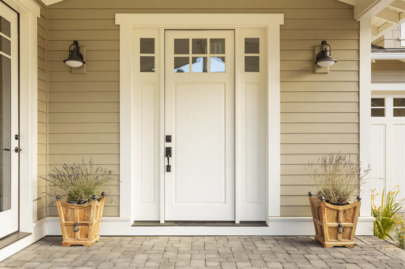 White wooden front door with small square decorative windows and flower pots